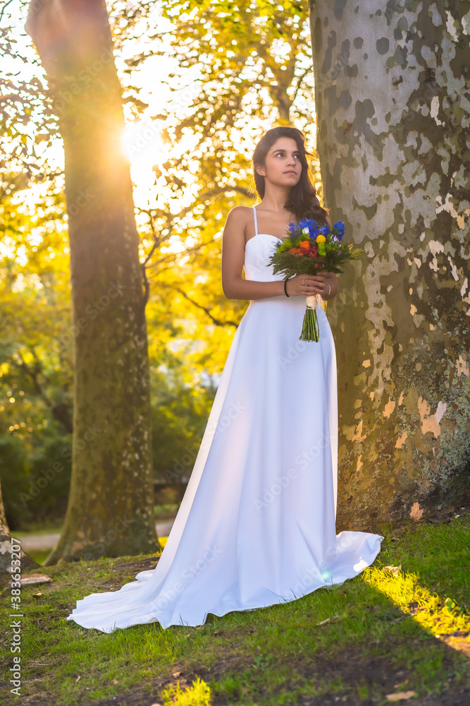 Caucasian brunette in long tail wedding dress at wedding celebration next to trees