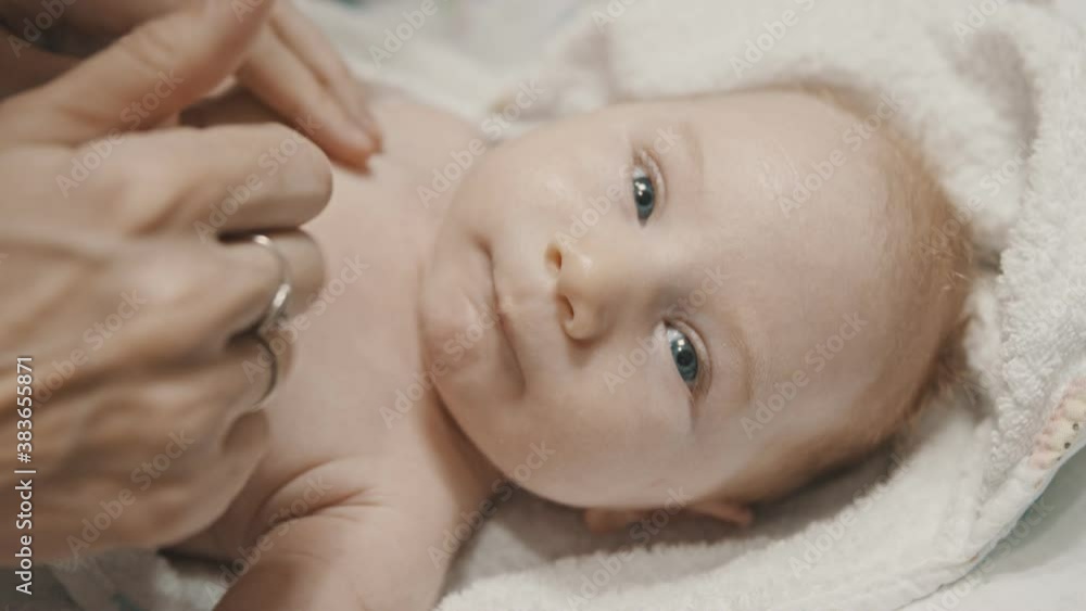 A little baby lying in bed and his mother applying cream in his neck A little baby lying in bed and his mother applying cream in his neck