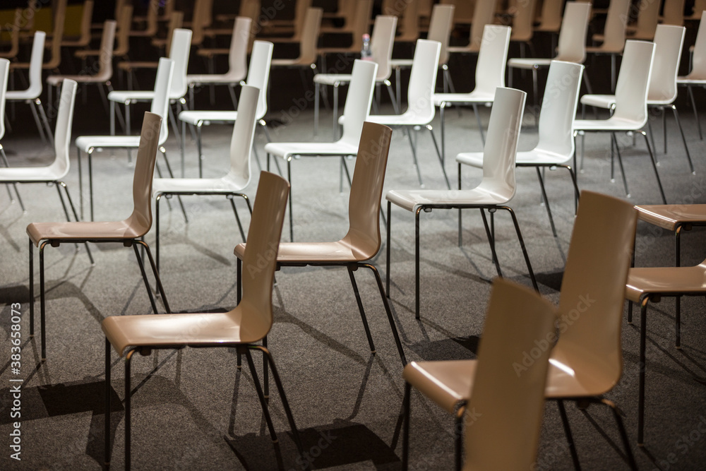 Group of empty white chairs arranged for social distance during indoor business event. COVID-19 health and safety measures during pandemic requires spacing between people Group of empty white chairs arranged for social distance during indoor business event. COVID-19 health and safety measures during pandemic requires spacing between people