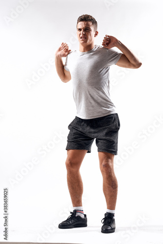 A sports man in shorts and a full-length T-shirt does exercises on a light background