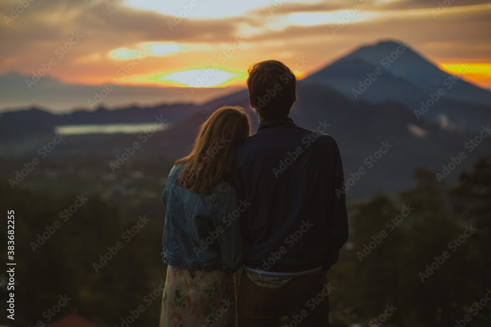 A loving couple man and woman stands near Batur volcano. Back view. Sunrise. Sunset. Tourists lovers on honeymoon enjoying summer vacation. Travel bloggers. Bali landmark A loving couple man and woman stands near Batur volcano. Back view. Sunrise. Sunset. Tourists lovers on honeymoon enjoying summer vacation. Travel bloggers. Bali landmark