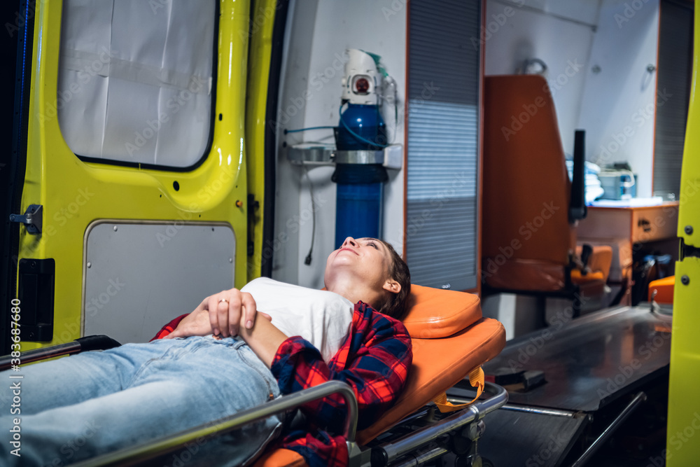 A young positive woman lying on a stretcher in front of an ambulance car. A young positive woman lying on a stretcher in front of an ambulance car.
