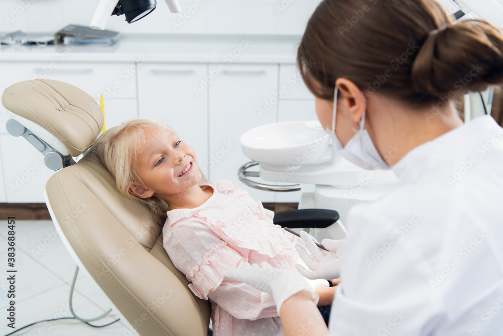 An experienced dentist is sitting near the girl trying to set up a contact with her to comfort her before the check up. An experienced dentist is sitting near the girl trying to set up a contact with her to comfort her before the check up.