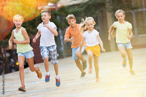 Group of smiling glad children running outdoors in city street on good weather