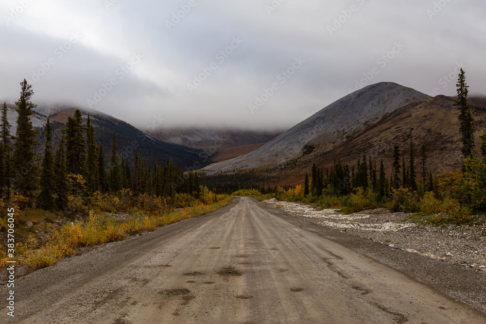 View of Scenic Road, Trees and Mountains on a Cloudy Fall Day in Canadian Nature. Taken near Tombstone Territorial Park, Yukon, Canada.