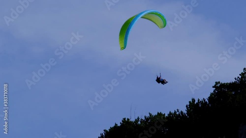 Bottom view of tandem paraglider with green and yellow parachute flying circes on a bright blue sunny day photo