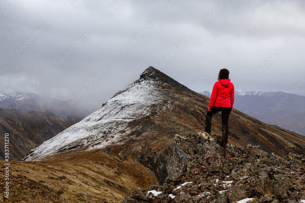 Woman Standing on Rocks looking at Scenic Mountain Peak in Canadian Nature. Season change from Fall to Winter. Taken in Tombstone Territorial Park, Yukon, Canada.
