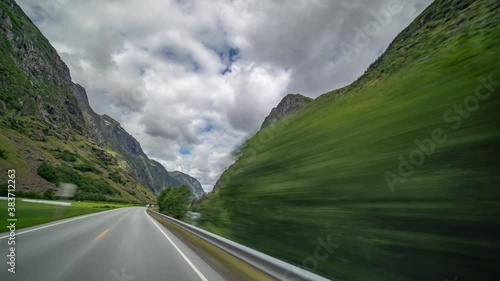 Drive on the E39 highway in Norway near Byrkjelo. The gray road going through the lush valley siding the river. Mountains fover on both sides of the road. Heavy, thick white-gray clouds flying above. photo