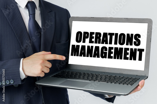 A businessman holds a laptop in his hands and shows on the screen with the text - OPERATIONS MANAGEMENT
