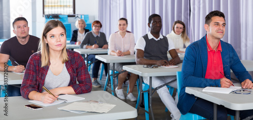 Multinational group of adult students listening teacher in classroom
