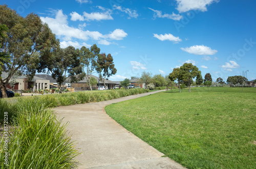 A curved pedestrian footpath/walkway in a suburban park with some modern Australian homes/houses in the distance. Background texture of a local park with large lawn and open space. Copy space for text