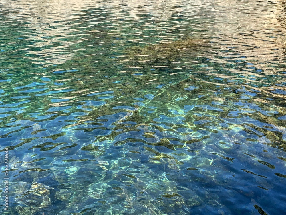 Turquoise blue transparent water in the sea,  light rippled crystal clear ocean waters with seaweed