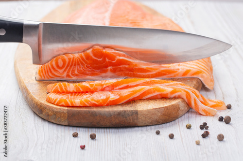 Knife cuts slices of fresh raw salmon