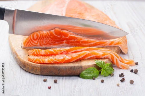 Knife cuts slices of fresh raw salmon