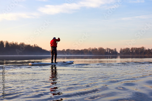 Water tourists is paddling on SUP (Stand up paddle board) at Danube river at cold season. Concept of water tourism, healthy lifestyle and recreation at winter