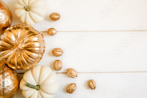 Pumpkins and nuts painted in gold on a white wooden background. Flat layout with space for text