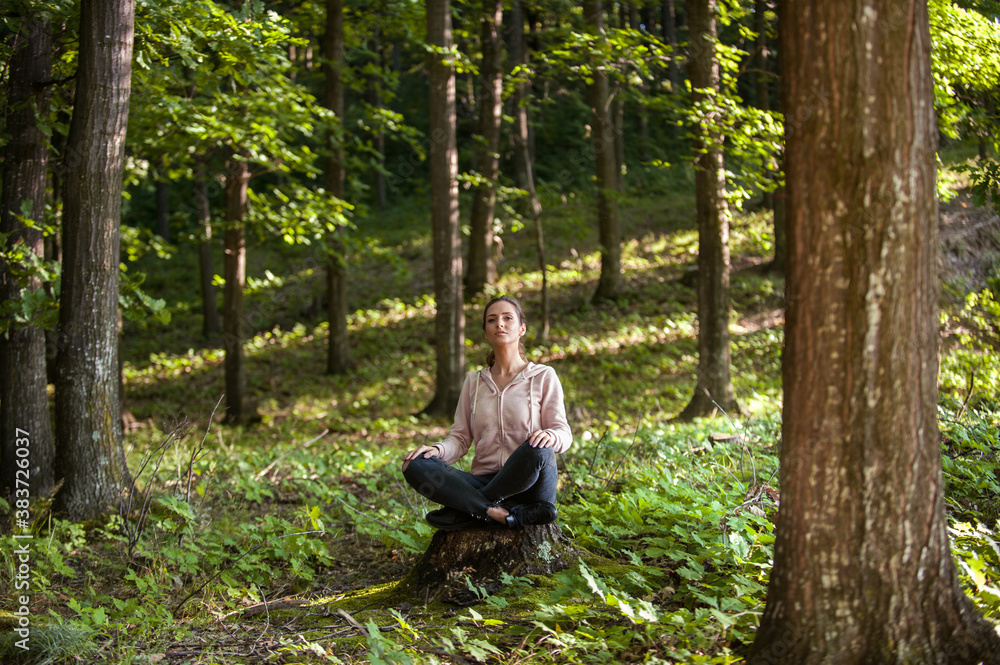 Young woman wearing yoga pants meditating in the woods on a sunny morning.
