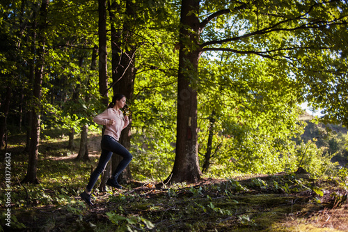 Young woman wearing yoga pants runing in the woods on a sunny morning.