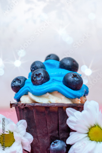 one sweet cupcake with blue cream and blueberries, decorated with flowers. close up