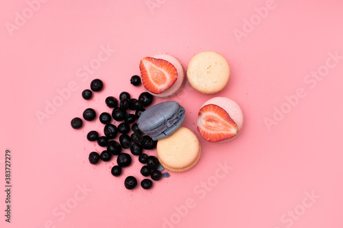 five macaroons of different colors are laid out in a circle and decorated with strawberries and blueberries on a pink background, top view