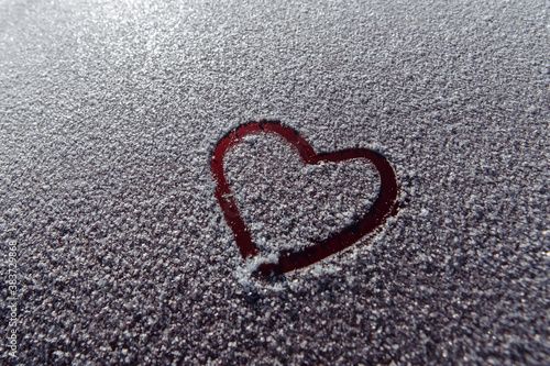 The heart shape is drawn with your finger on a red background and snow. High quality photo