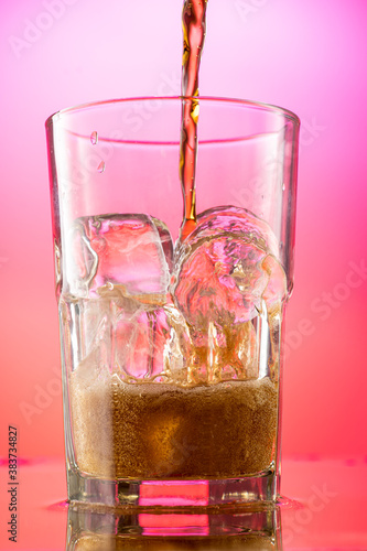 pour cola into a glass with pieces of pure real ice on a red purple gradient background