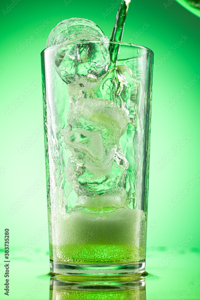 pouring green tarragon lemonade into glass with pieces of pure real ice on green gradient background pouring green tarragon lemonade into glass with pieces of pure real ice on green gradient background