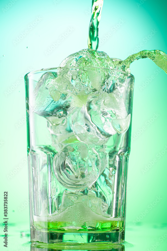 pouring green tarragon lemonade into glass with pieces of pure real ice on green gradient background pouring green tarragon lemonade into glass with pieces of pure real ice on green gradient background
