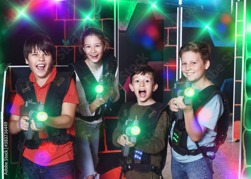 Group portrait of cheerful positive smiling teenagers with laser guns having fun on dark lasertag arena