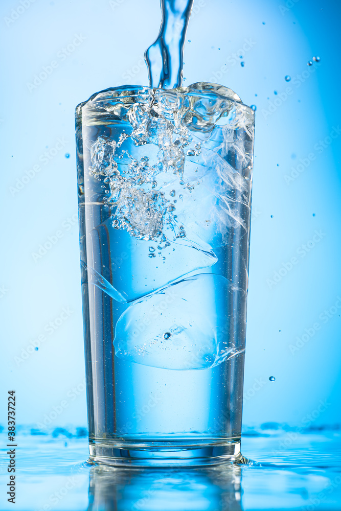 pour clear water into a glass with chunks of pure real ice on a blue gradient background