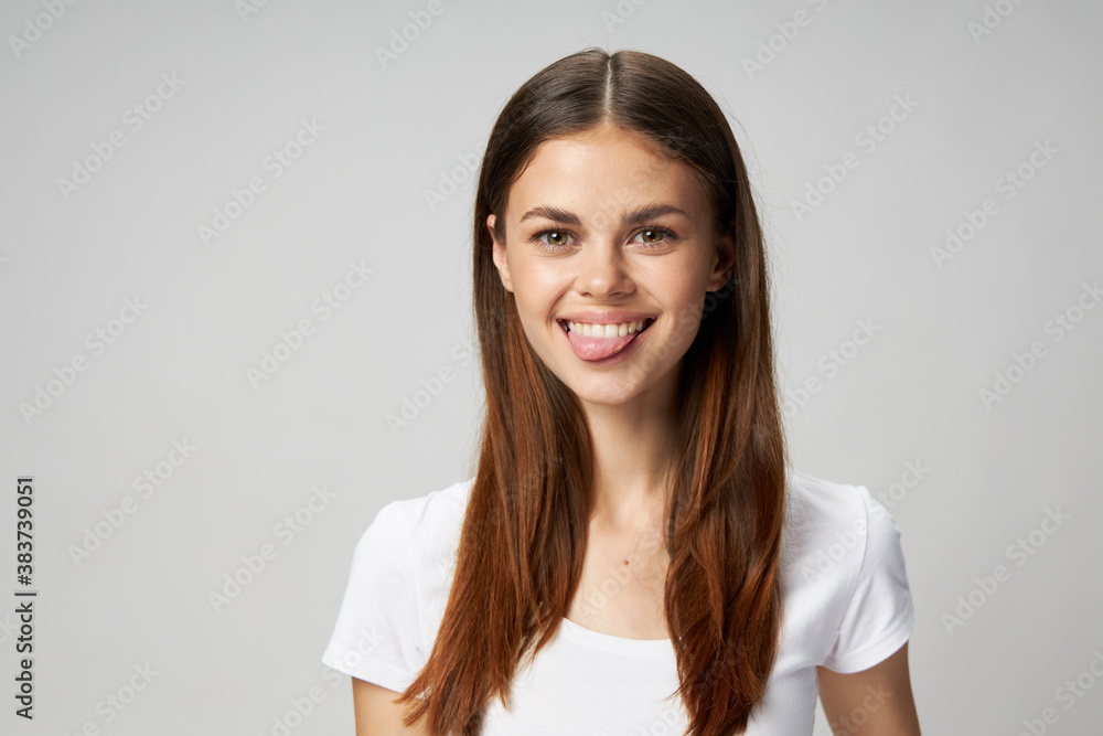 Happy woman shows tongue in a white T-shirt on a light background Happy woman shows tongue in a white T-shirt on a light background