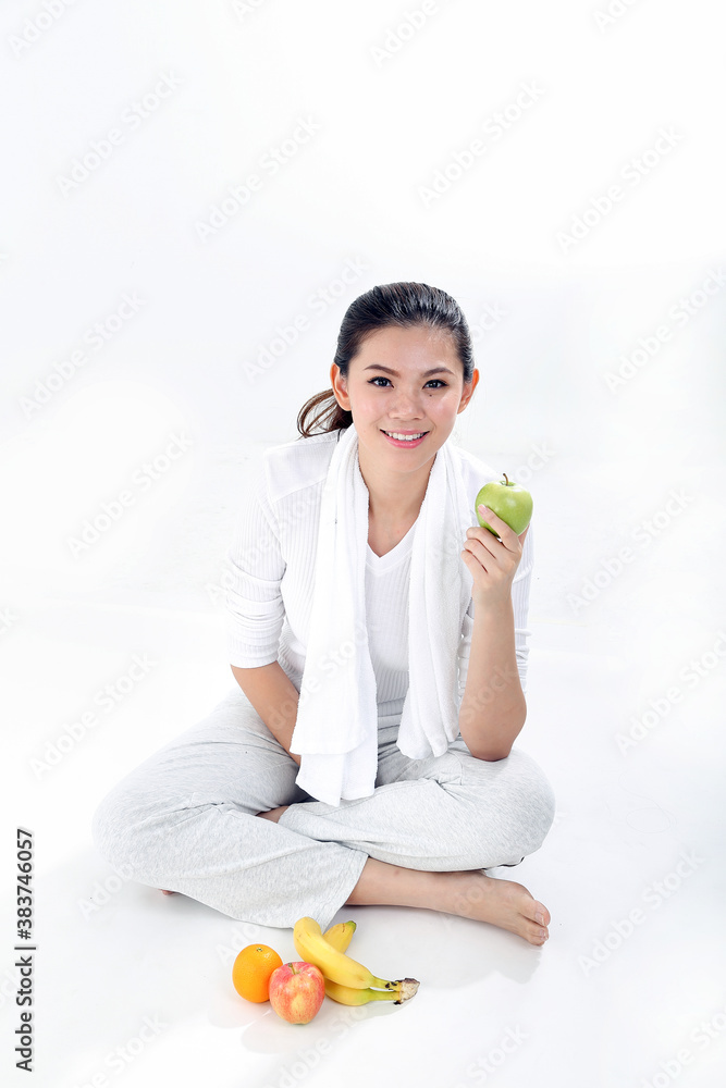 Beautiful young south east Asian Chinese healthy workout exercise sit on floor holding green apple look at camera on white background