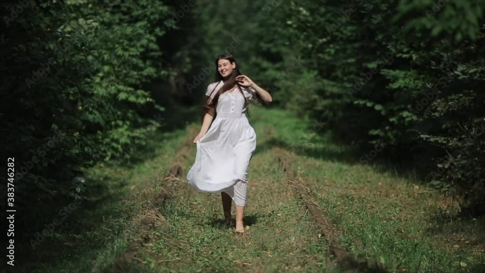 A cheerful young girl in a long white dress runs along the sleepers of an old overgrown railroad in a summer forest. Front view. Close-up. Slow motion A cheerful young girl in a long white dress runs along the sleepers of an old overgrown railroad in a summer forest. Front view. Close-up. Slow motion