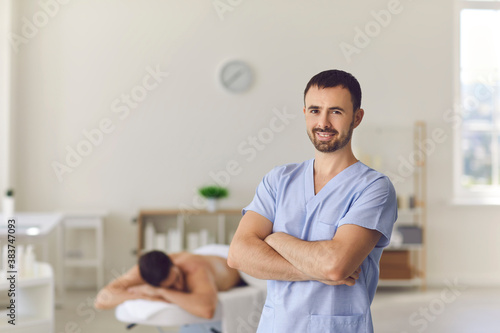 Smiling professional masseur or manual therapist standing arms crossed in his massage room photo