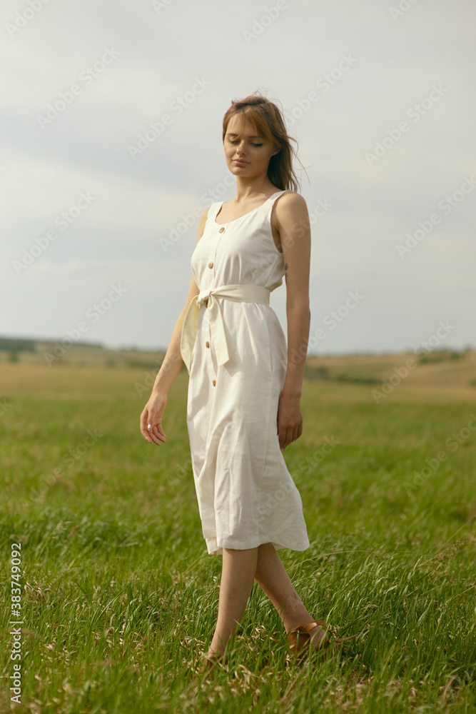 Nice picnic on the grass. Young beautiful woman in the middle of green field. Summer landscape, good weather. Windy day with sun and clouds. Cotton white suit eco style. Nice picnic on the grass. Young beautiful woman in the middle of green field. Summer landscape, good weather. Windy day with sun and clouds. Cotton white suit eco style.