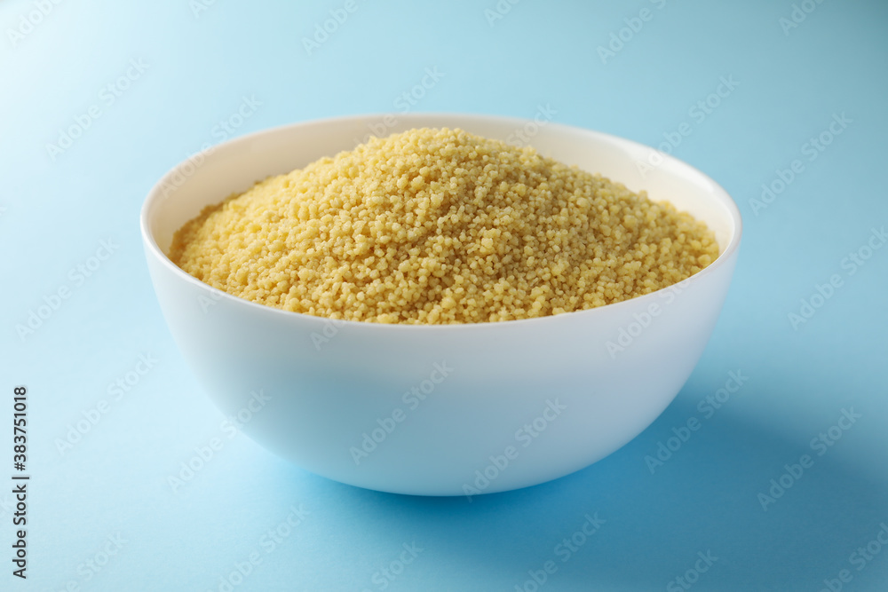 Bowl with raw couscous on blue background Bowl with raw couscous on blue background