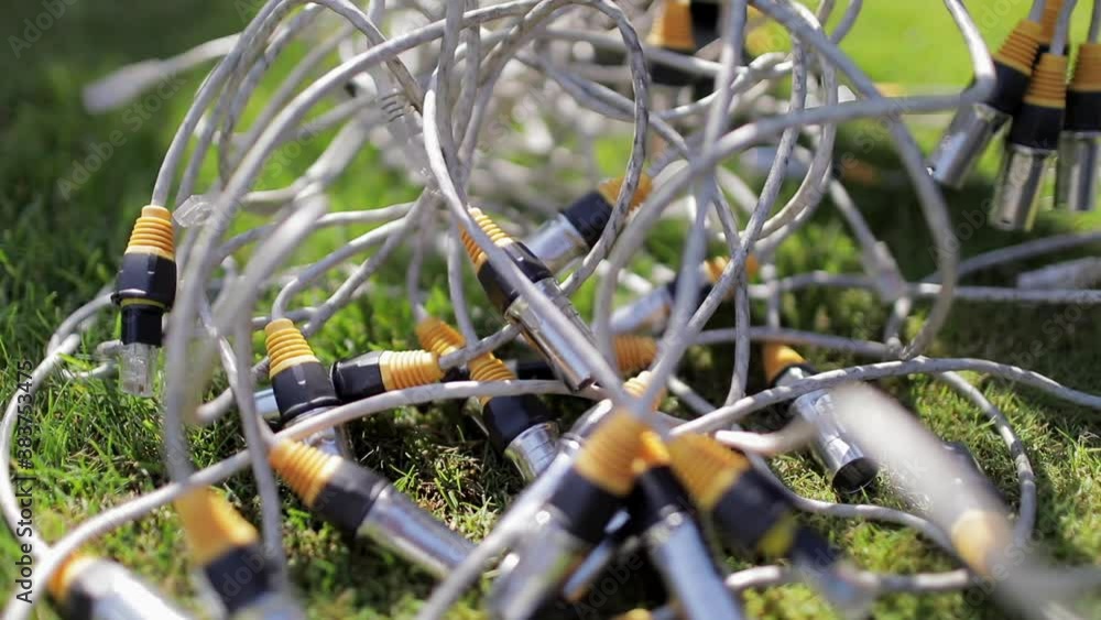 Close up of tangled white wires with jack plugs on the green grass, which the person is trying to untangle with his hand. Close up of tangled white wires with jack plugs on the green grass, which the person is trying to untangle with his hand.