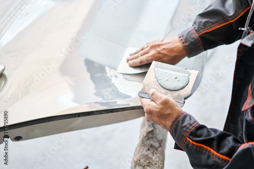 Repairing car body, Application putty close up. The mechanic repair the car. Work after the accident by working sanding primer before painting.
