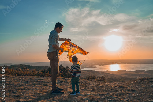 A little boy and his father play flying kite in nature at sunset.