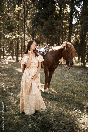 A beautiful young girl dressed in a dress stands near a horse in the forest © Дмитрий Ткачук