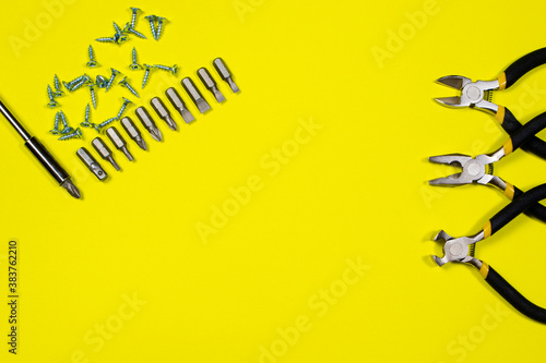 Screwdriver with set of nozzles, self-cutters and other inturments - pliers, cutters, tongs on a yellow background with space for text
