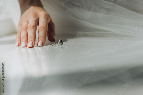 Close up of the hand of the bride with manicure and a vintage ring with a blue diamond on the windowsill.