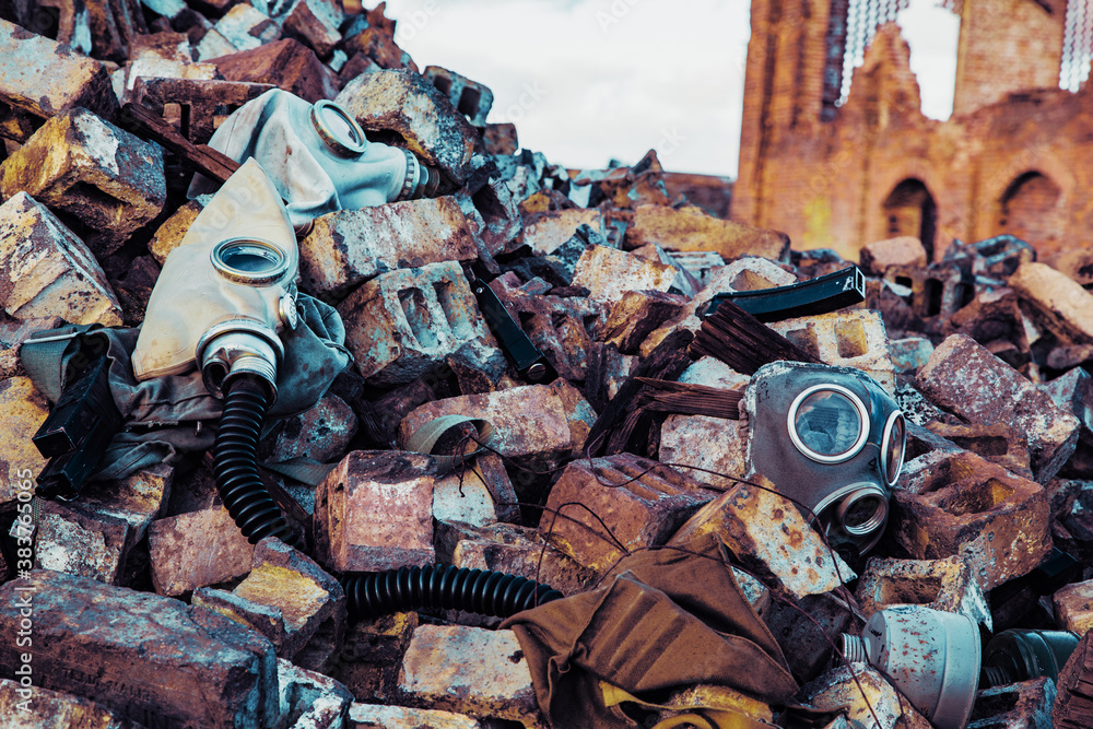 Varias mascaras de gas y cartuchos en escombros con edificio derruido en fondo