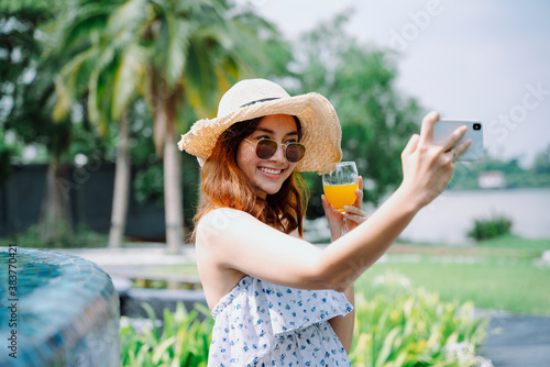 Asian woman traveler wear hat and sunglasses taking selfie with orange juice.
