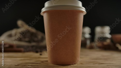 Craft disposable cup for hot drinks presentation. Tea or coffee, espresso, latte, cappuccino for take away. Wood table, coffee traditional beans and spices on the background. Zoom in. Focused on cup
