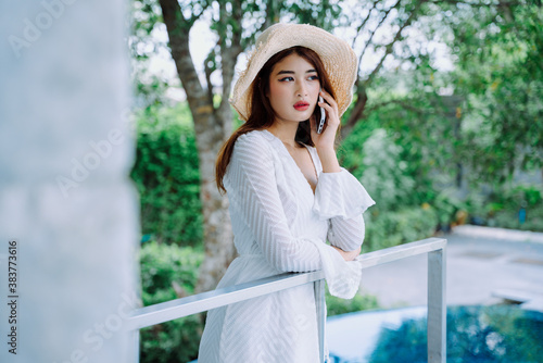 Asian woman traveler wear hat talking on the phone in resort hotel.