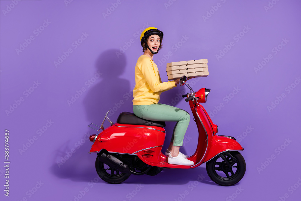 Full size profile side photo of shocked courier girl drive motor bike hold pizza box isolated on violet color background Full size profile side photo of shocked courier girl drive motor bike hold pizza box isolated on violet color background
