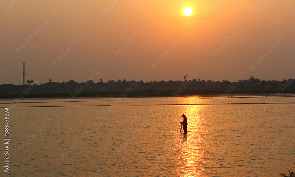 Fisherman throwing net in water with beautiful sunset in the background
