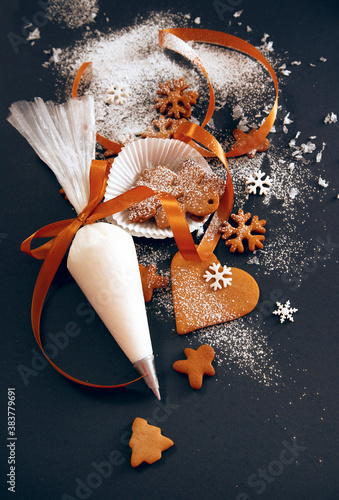 Christmas gingerbread cookies with confectionery mastic snowflakes and pastry bag with icing on black background, view from above. Holiday food, homemade baking, Christmas and New Year traditions.
