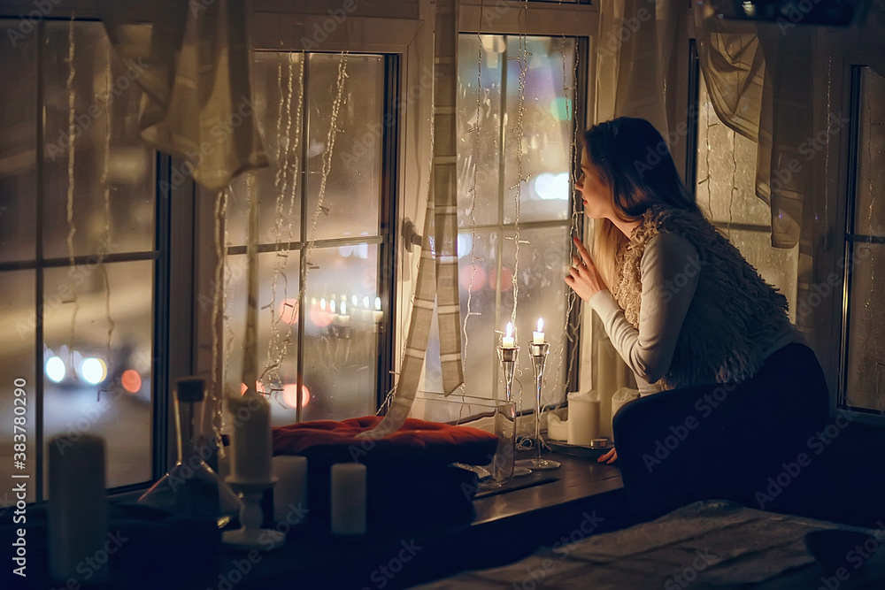 Christmas evening girl / beautiful young adult model, dreams and makes wishes at the candles in the New Year's Eve